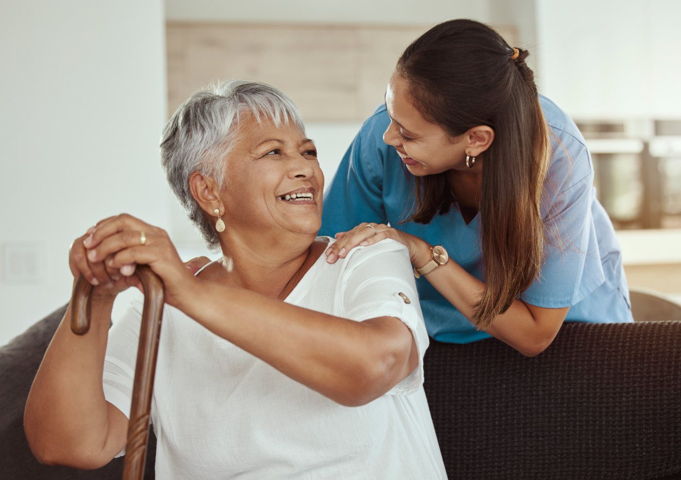 Caregiver assisting senior woman with cane while both smile warmly