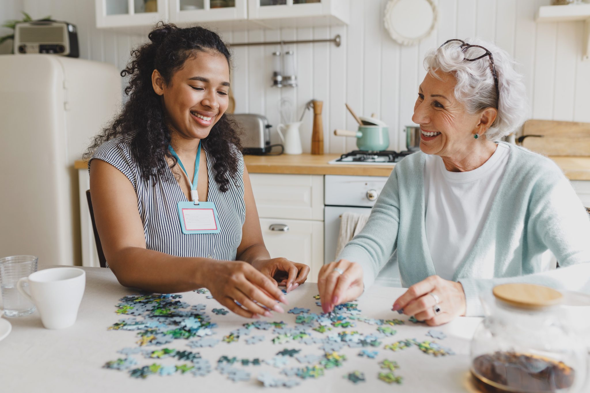 Young caregiver and senior woman solving puzzle together at kitchen table