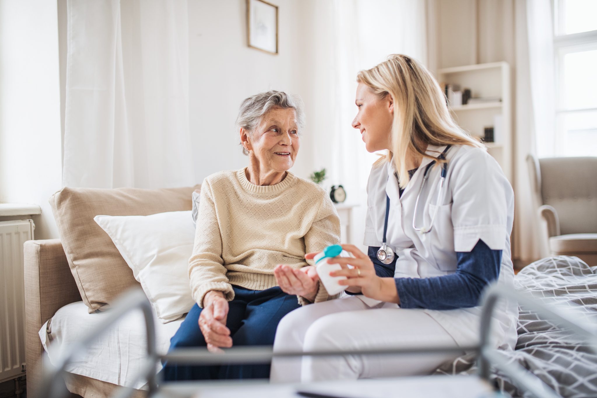 Healthcare professional showing medication bottle to elderly patient during home visit