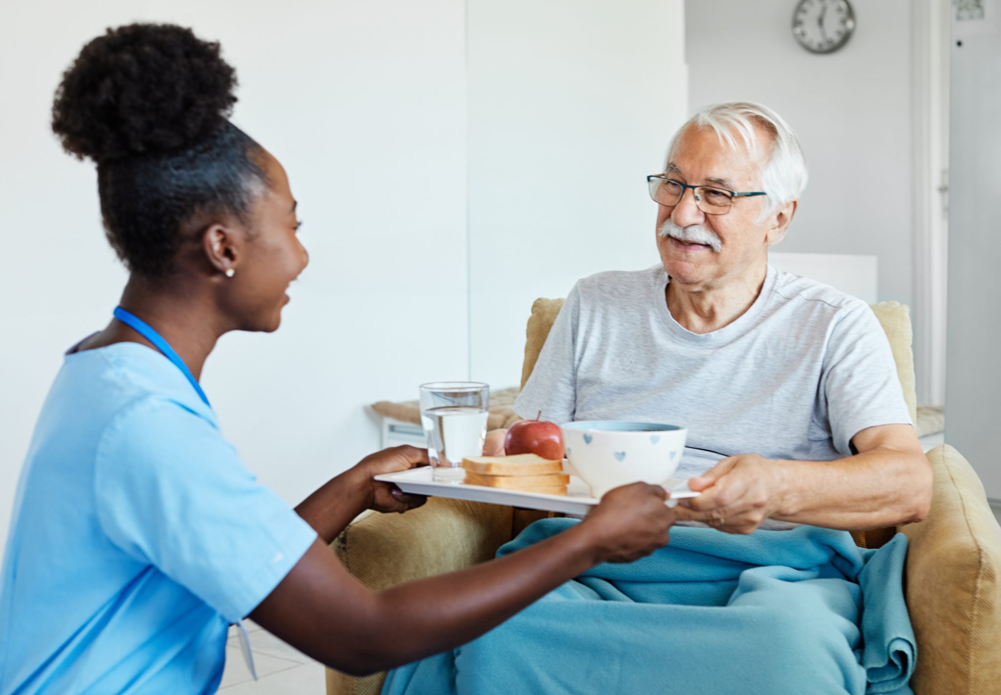 Healthcare worker serving meal to senior man in home setting